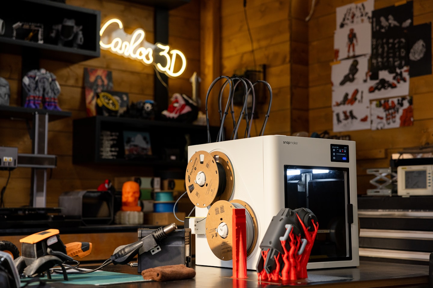 A modern 3D printer creates a red object on a workbench.